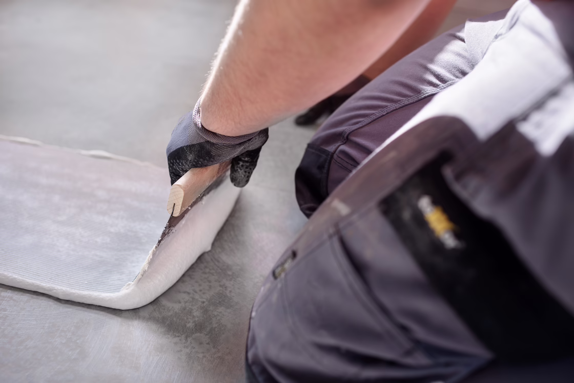 Installer applying adhesive to a subfloor with a trowel, preparing the surface for floor covering installation.