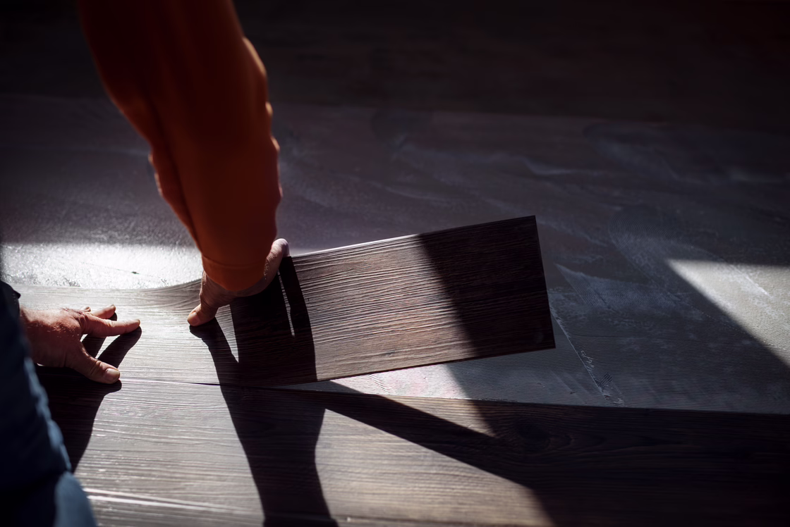 Installer positioning a dark wood-look LVT plank on a prepared subfloor, aligning it precisely before installation.